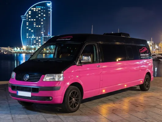 Minivan Volkswagen rosa y negra por la ciudad de noche